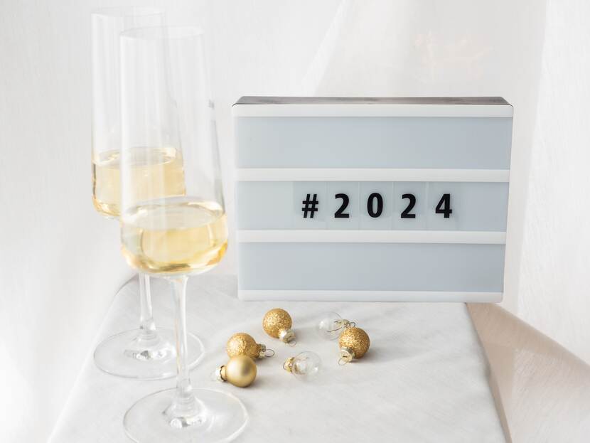 Twee glazen met champagn en wat kerstballen op de voorgrond en daarachter een bord met de cijfers 2024