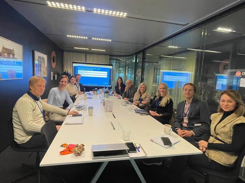 Diverse medewerkers op het gebied van leren en ontwikkelen zitten aan een lange tafel aan weerszijden en kijken in de camera