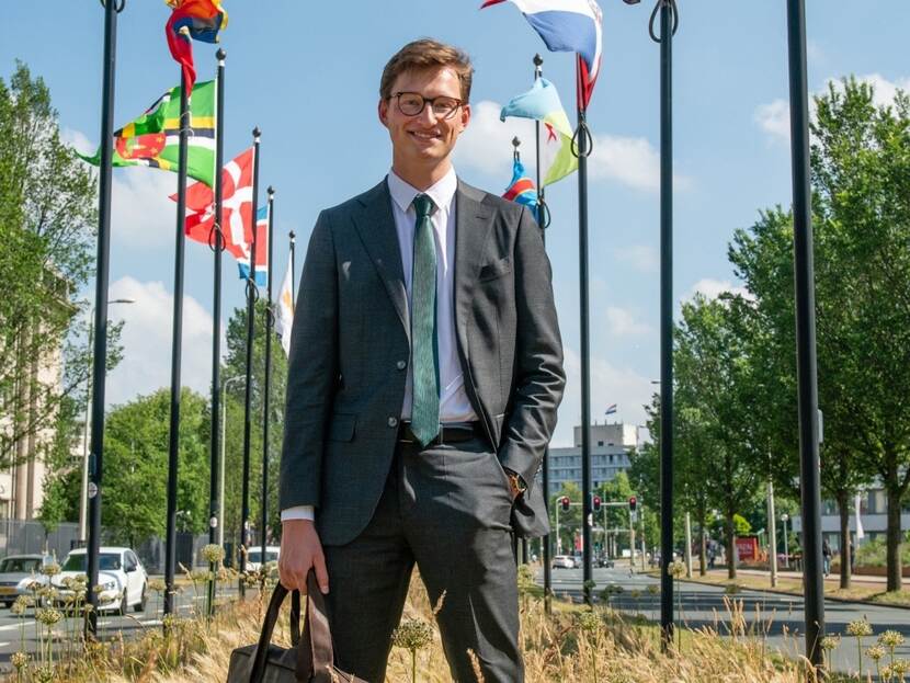 Portretfoto van Bart van der Meer. Hij staat in het midden en achter hem zie je links een rechts een rij vlaggen