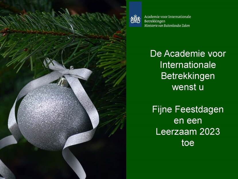 Links hangt een zilveren kerstbal met een zilveren strik aan een dennentak en rechts staat de kerstwens van de academie op een groene achtergrond